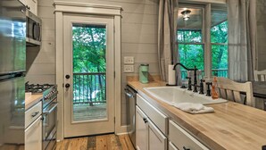 A kitchen with a wooden countertop, stainless steel appliances, a window with a view of greenery, and a door leading to an outdoor deck. - Rustic-chic Riverfront Home w/ Dock, Deck & Canoes (Tallassee)