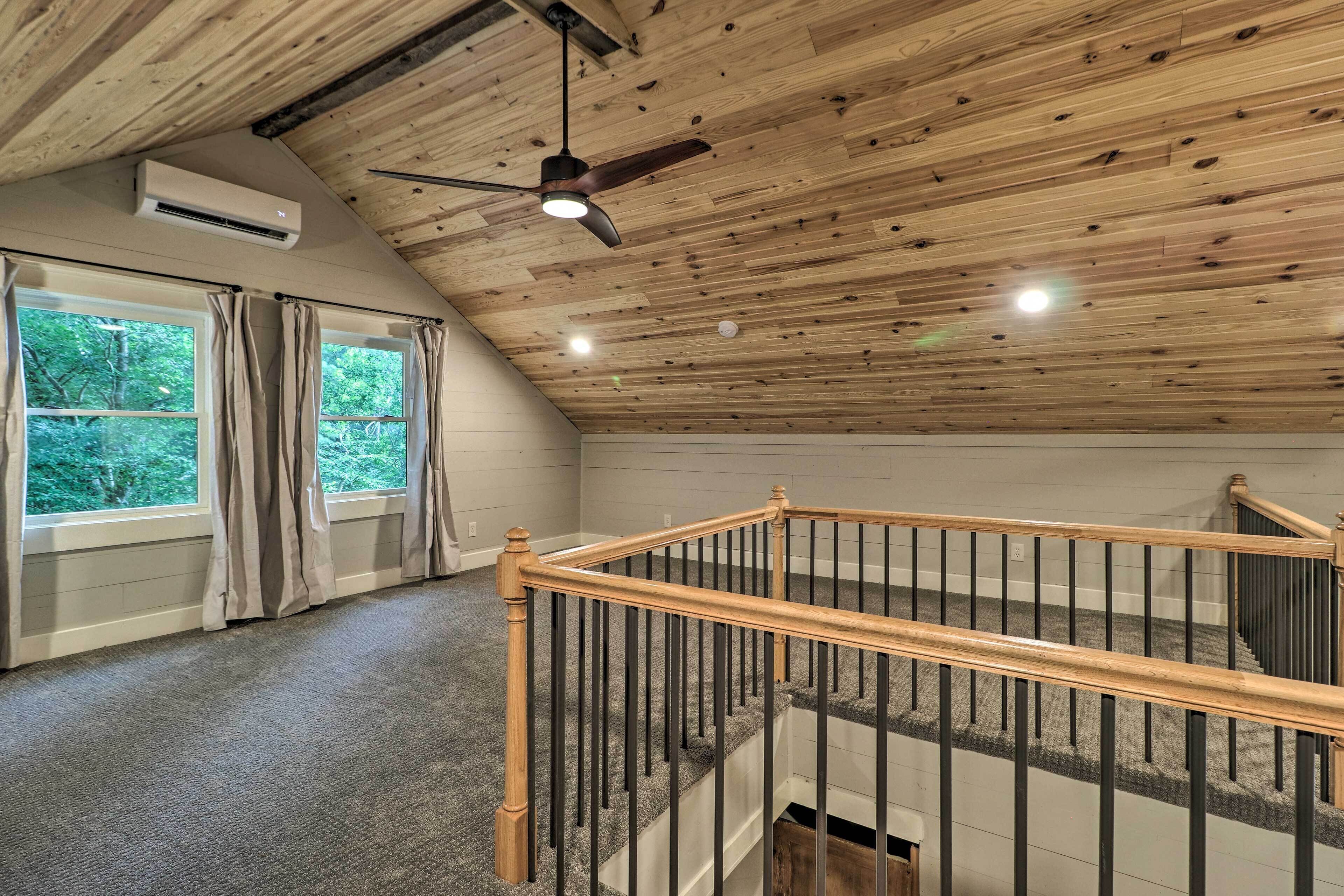 Une pièce avec des poutres apparentes en bois au plafond, un ventilateur de plafond et un escalier doté d’une rampe en bois.