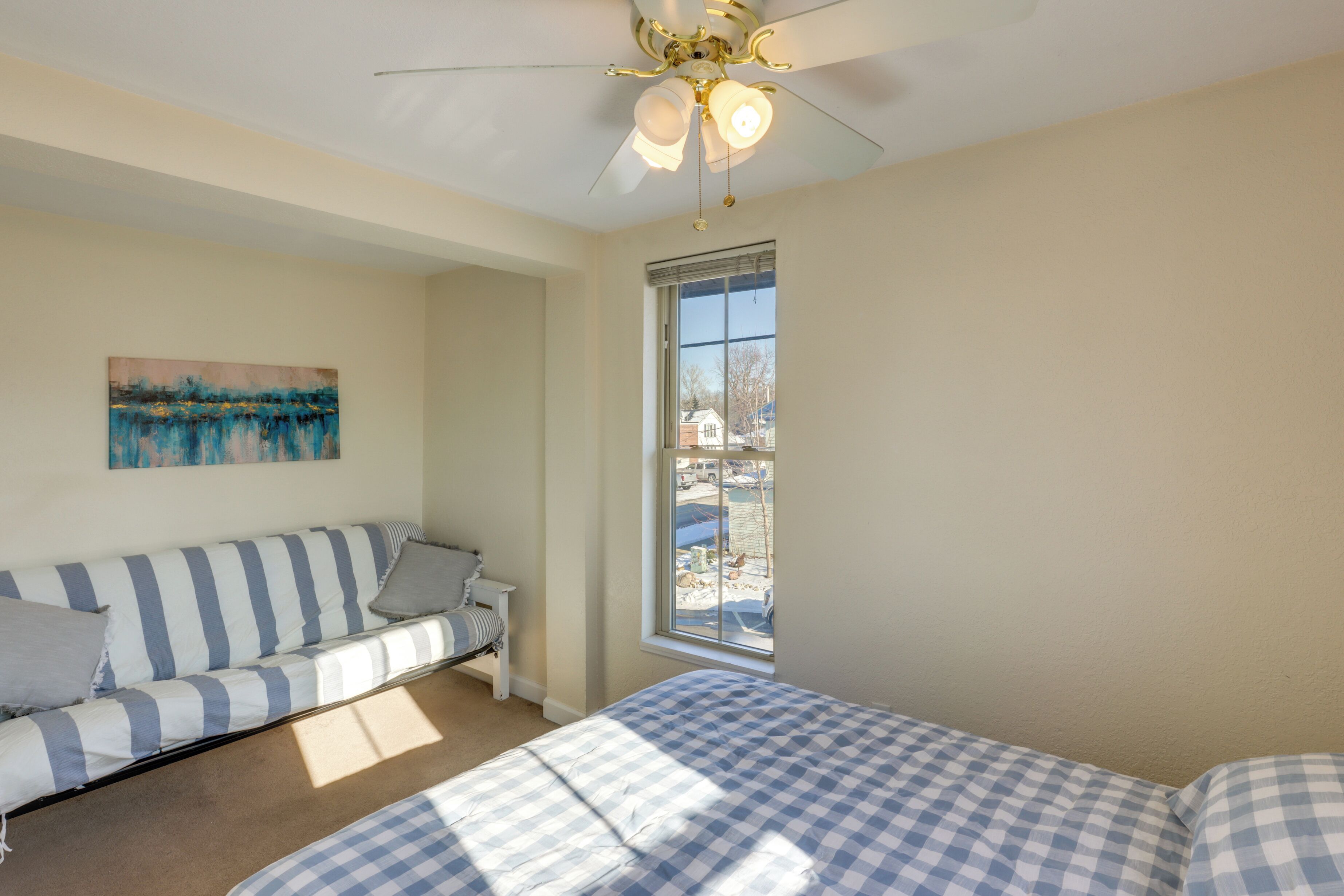 Une chambre à coucher avec un lit, une fenêtre, un ventilateur de plafond et un tableau accroché au mur.