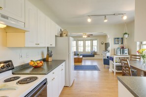 A modern kitchen with white cabinets, a stove, and a microwave. There is a dining area with a table and chairs, and a living room with a sofa and a coffee table. - Delafield Vacation Rental Near Lakes & Parks! (Delafield)