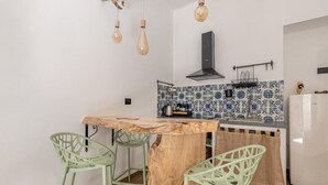 Una cocina con una isla de madera, dos sillas verdes, lámparas colgantes, una campana extractora negra y un backsplash de azulejos.