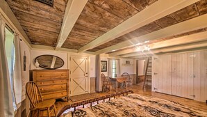 A rustic bedroom with wooden floors, a large fur rug, a wooden dresser, a chair, and a dining table with chairs. - Remote 1901 Studio Cabin w/ Loft - Pets Allowed! (Allenwood)