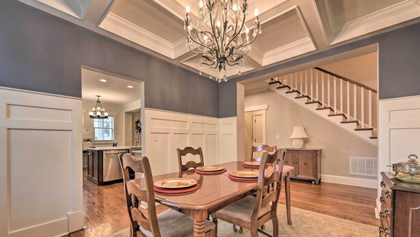 A dining area with a wooden table set for four, surrounded by chairs. A chandelier hangs from the ceiling, and a staircase is visible in the background. - 2 Mi to Dtwn: Home in Noda District Near Unc! (Charlotte)