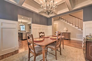 A dining area with a wooden table set for four, surrounded by chairs. A chandelier hangs from the ceiling, and a staircase is visible in the background. - 2 Mi to Dtwn: Home in Noda District Near Unc! (Charlotte)