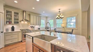 A spacious kitchen with white cabinetry, a large island, and a stainless steel range hood.