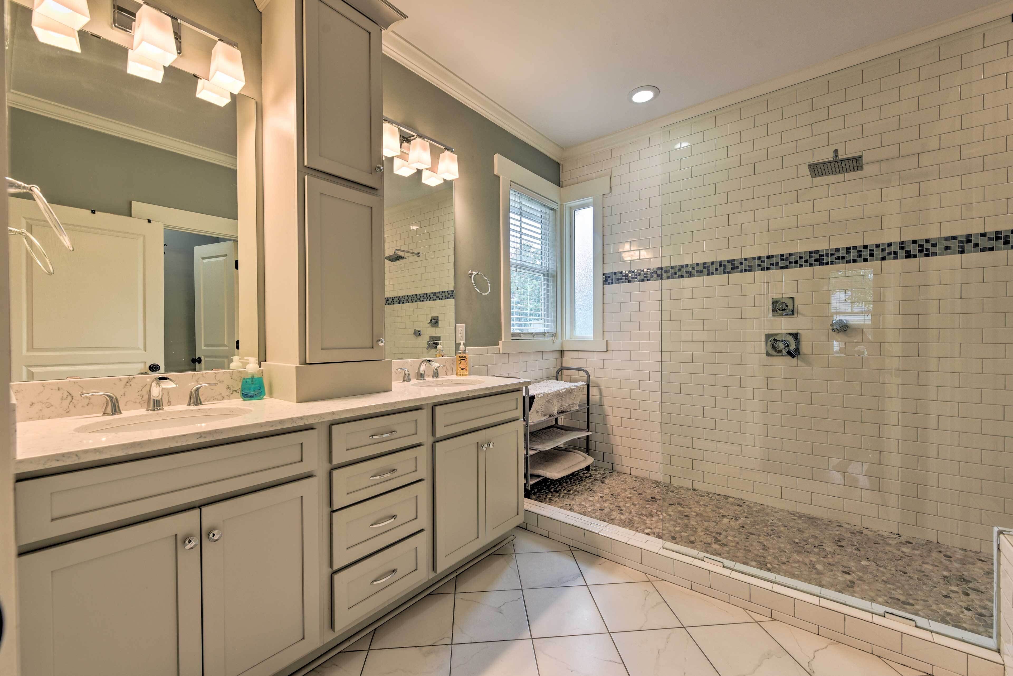 A bathroom with a large mirror, two sinks, a shower, and a tiled floor.