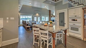 A spacious kitchen with a large island, white cabinetry, and a stone fireplace. - Lavish Lake House, Near Vineyards + Marinas! (Granbury)
