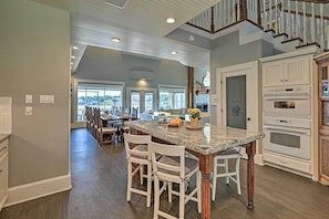 A spacious kitchen with a large island, white cabinetry, and a stone fireplace. - Lavish Lake House, Near Vineyards + Marinas! (Granbury)