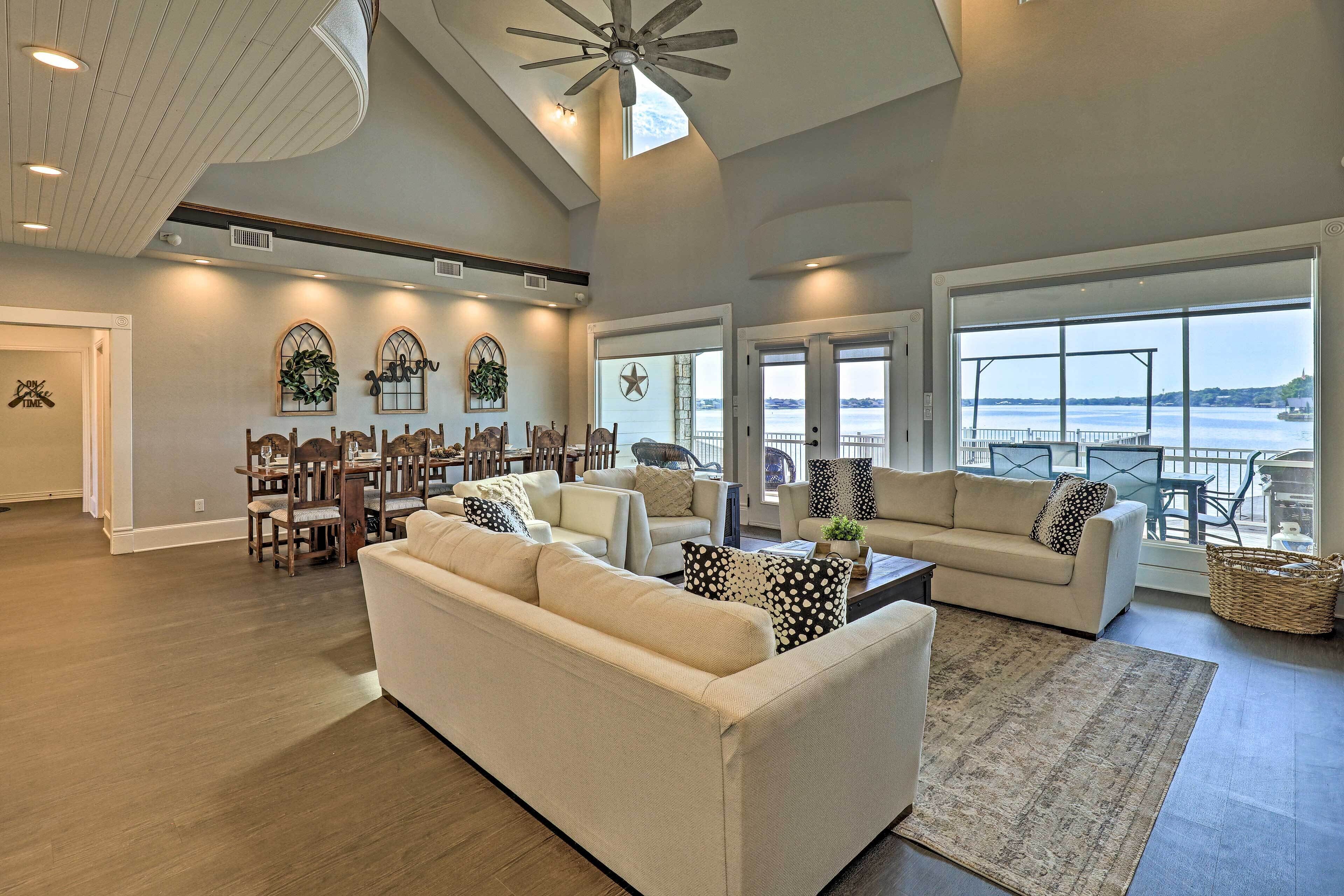 A spacious living room with a high ceiling, large windows, and a view of the water.
