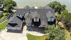 A large house with a stone tower, a covered porch, and a dock extending into a lake. - Lavish Lake House, Near Vineyards + Marinas! (Granbury)
