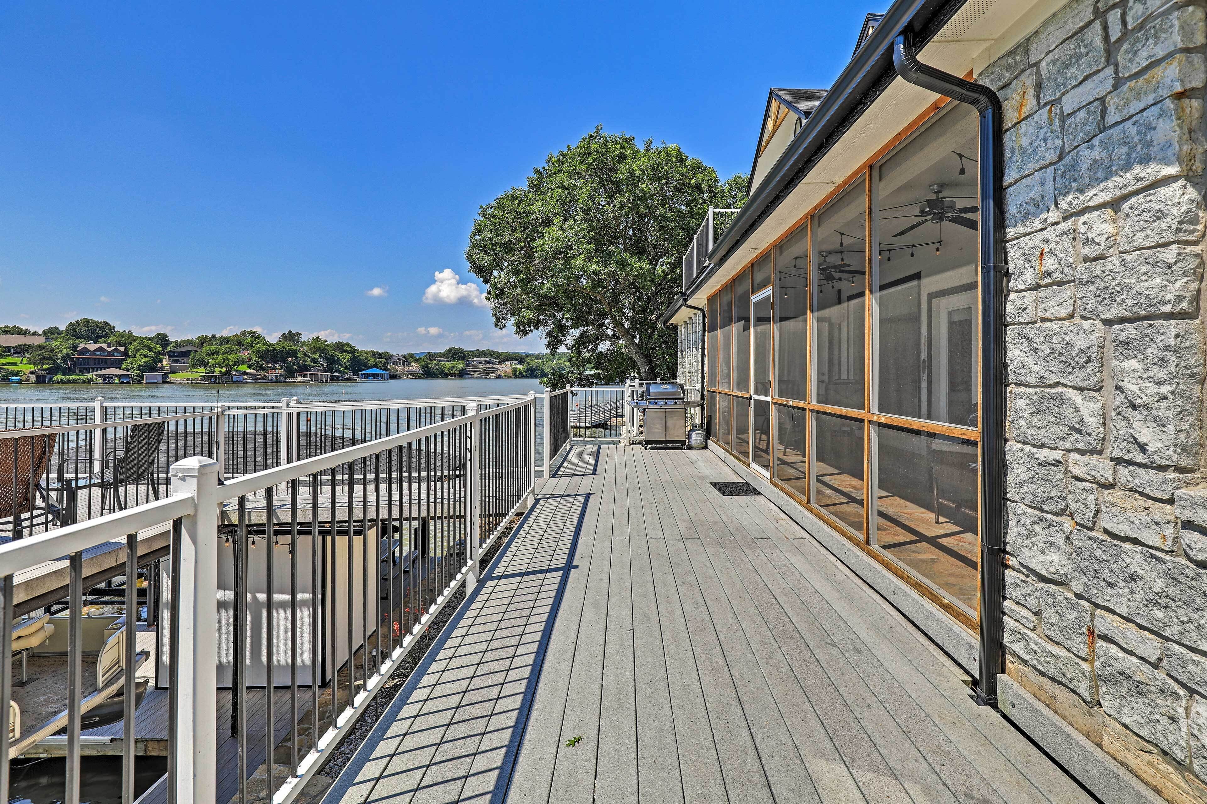 A wooden deck with a railing overlooking a body of water, a stone wall, and a large window.