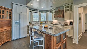 A kitchen with a central island, white cabinetry, and a wooden cabinet to the left. - Lavish Lake House, Near Vineyards + Marinas! (Granbury)