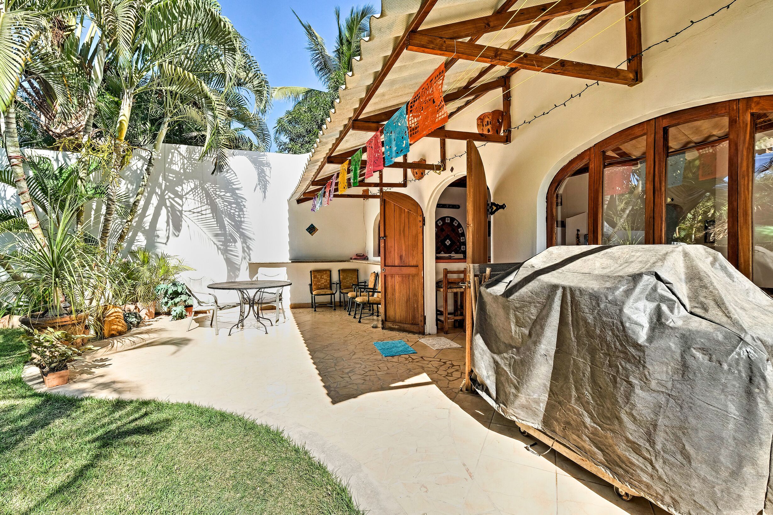 A covered patio with a barbecue, outdoor seating, and a view of the surrounding greenery.