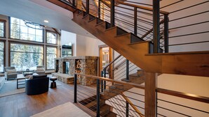 Un vaste espace de vie agrémenté d’un escalier en bois, de grandes fenêtres et d’une cheminée en pierre.