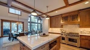 Une cuisine moderne avec des meubles en bois, un îlot en marbre, des appareils électroménagers en acier inoxydable et de grandes fenêtres.