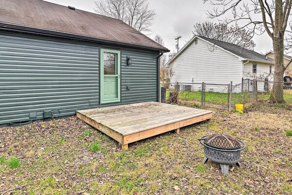 A green metal shed with a green door, a wooden deck, and a metal fire pit.