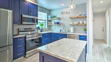 A modern kitchen with dark blue cabinets, stainless steel appliances, and a marble countertop.