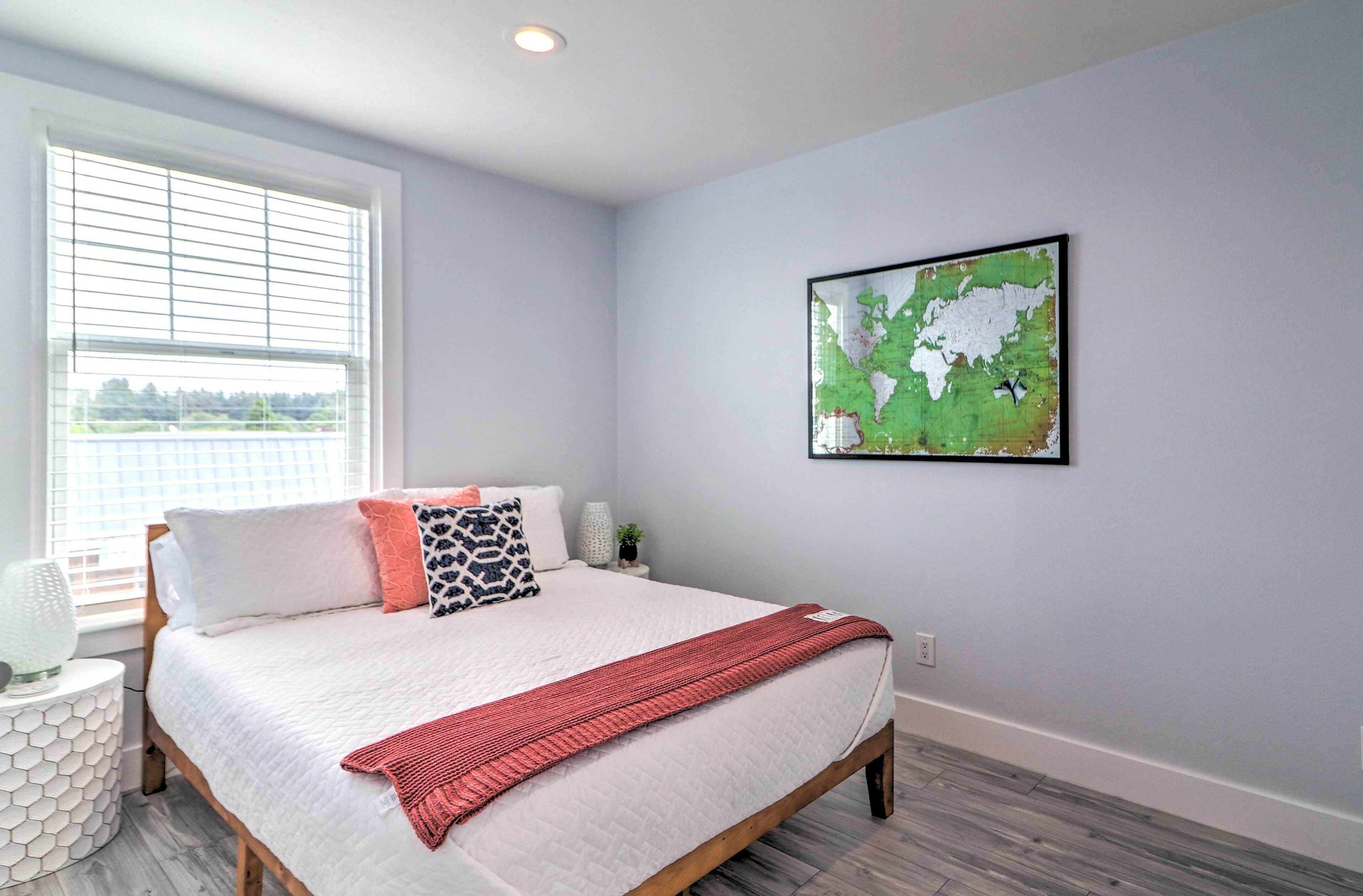A bedroom with a bed, a window, a wall-mounted map, and a small side table with a lamp.
