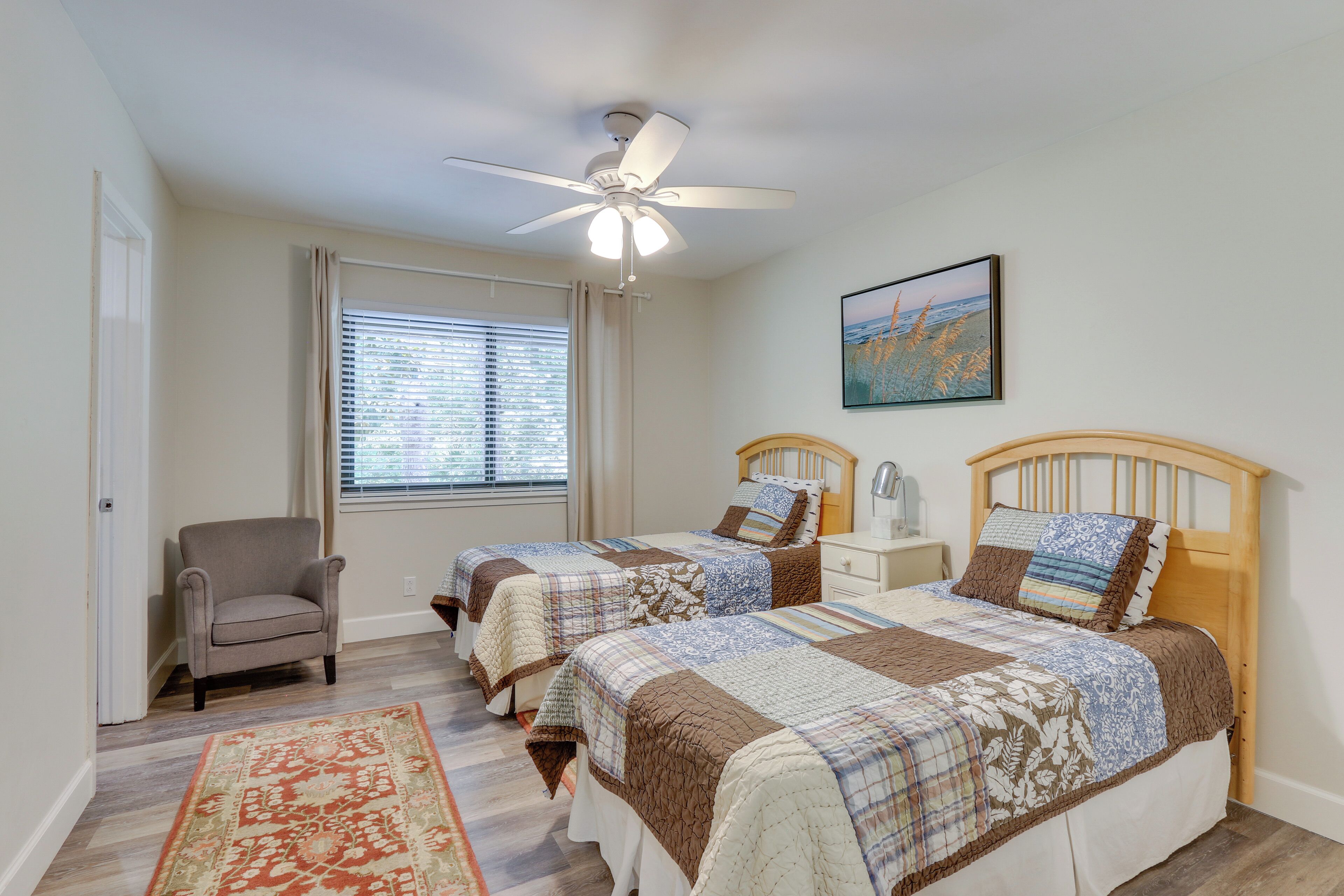 A bedroom with two beds, a ceiling fan, a window with blinds, a chair, and a rug.