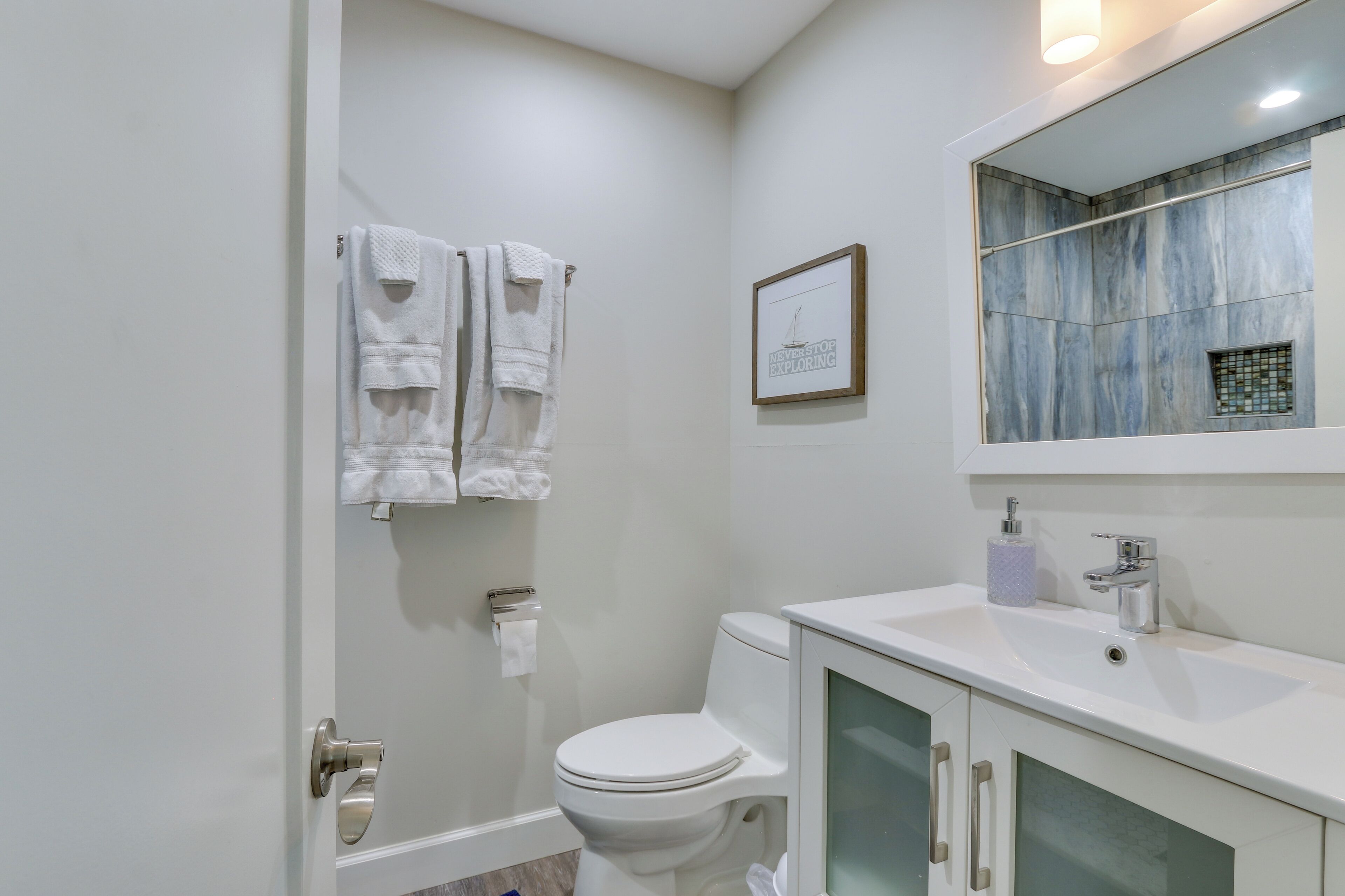 Een badkamer met een toilet, een wastafel, een handdoekrek met handdoeken, een lijst met een afbeelding en een spiegel die de badkamer weerspiegelt.