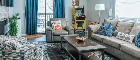 A living room with a sofa, armchair, coffee table, and a game machine.