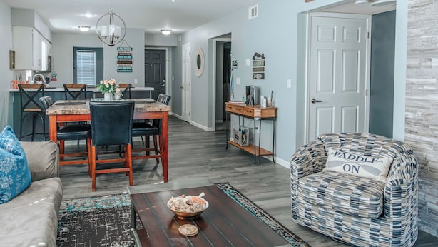 A living room with a sofa, a coffee table with a bowl, a patterned armchair, and a dining area with a table and chairs. - Updated Branson Condo w/ Indoor Pool Access! (Branson)