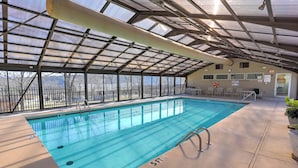 An indoor swimming pool with clear blue water, surrounded by a covered area with a metal roof and glass walls. - Updated Branson Condo w/ Indoor Pool Access! (Branson)