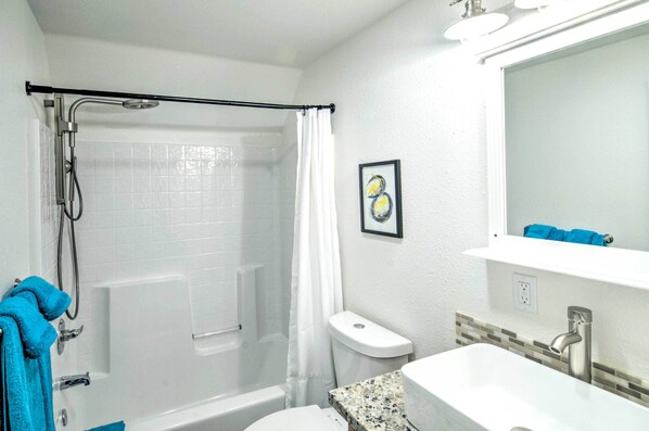 A bathroom with a shower, toilet, sink, and a framed picture on the wall.
