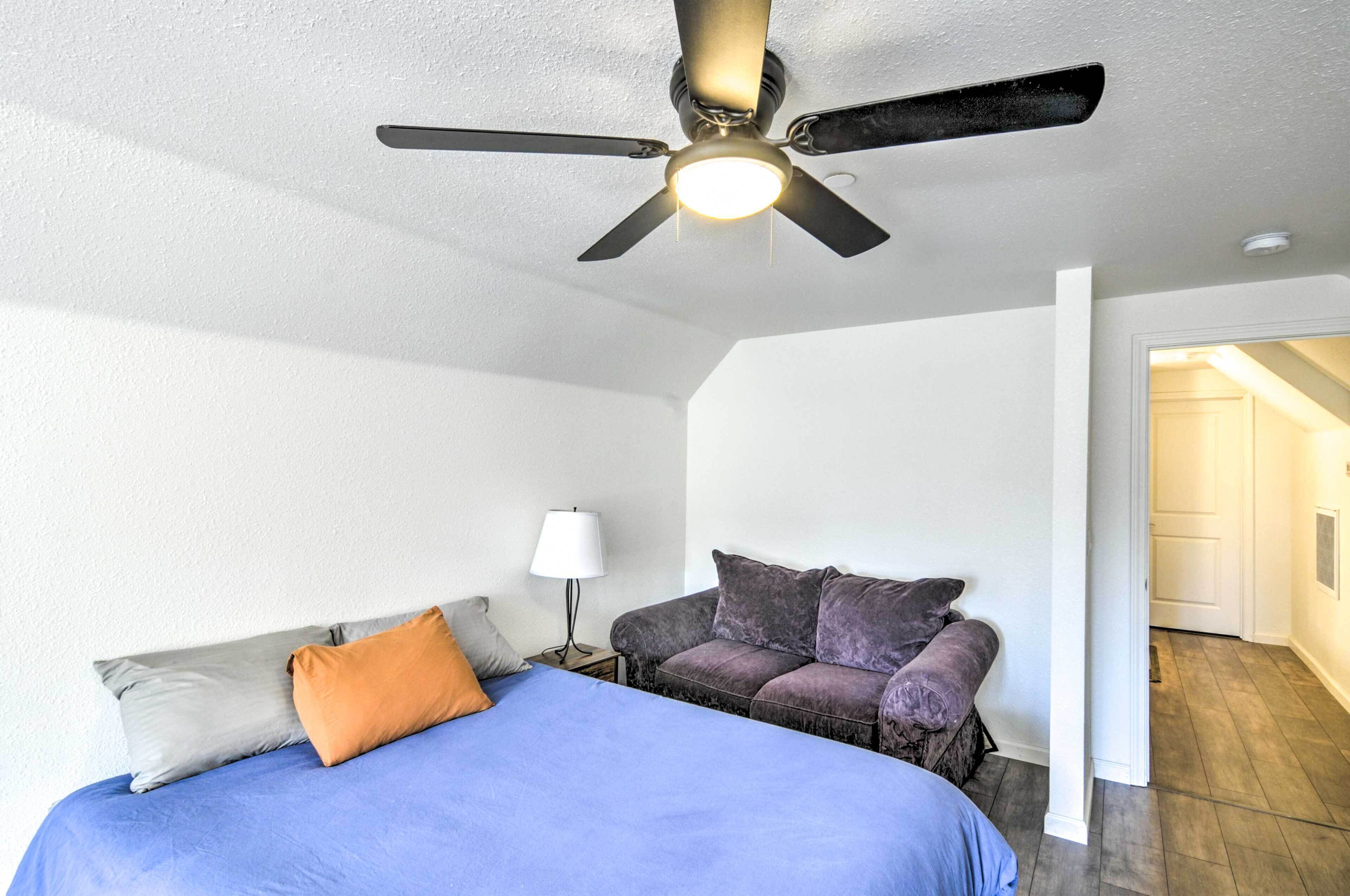 A bedroom with a bed, a nightstand, a lamp, a sofa, and a ceiling fan.