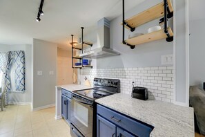 A modern kitchen with a built-in oven, a stove, and a microwave. There are wooden shelves above the stove and a window with patterned curtains. - Charming Jacksonville Abode w/ Patio! (Jacksonville)