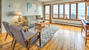 A living room with a sofa, chairs, a coffee table, and a TV stand. There is a large window with a view of the beach. - Anchor Bay Getaway on Lake St Clair With Dock! (New Baltimore)