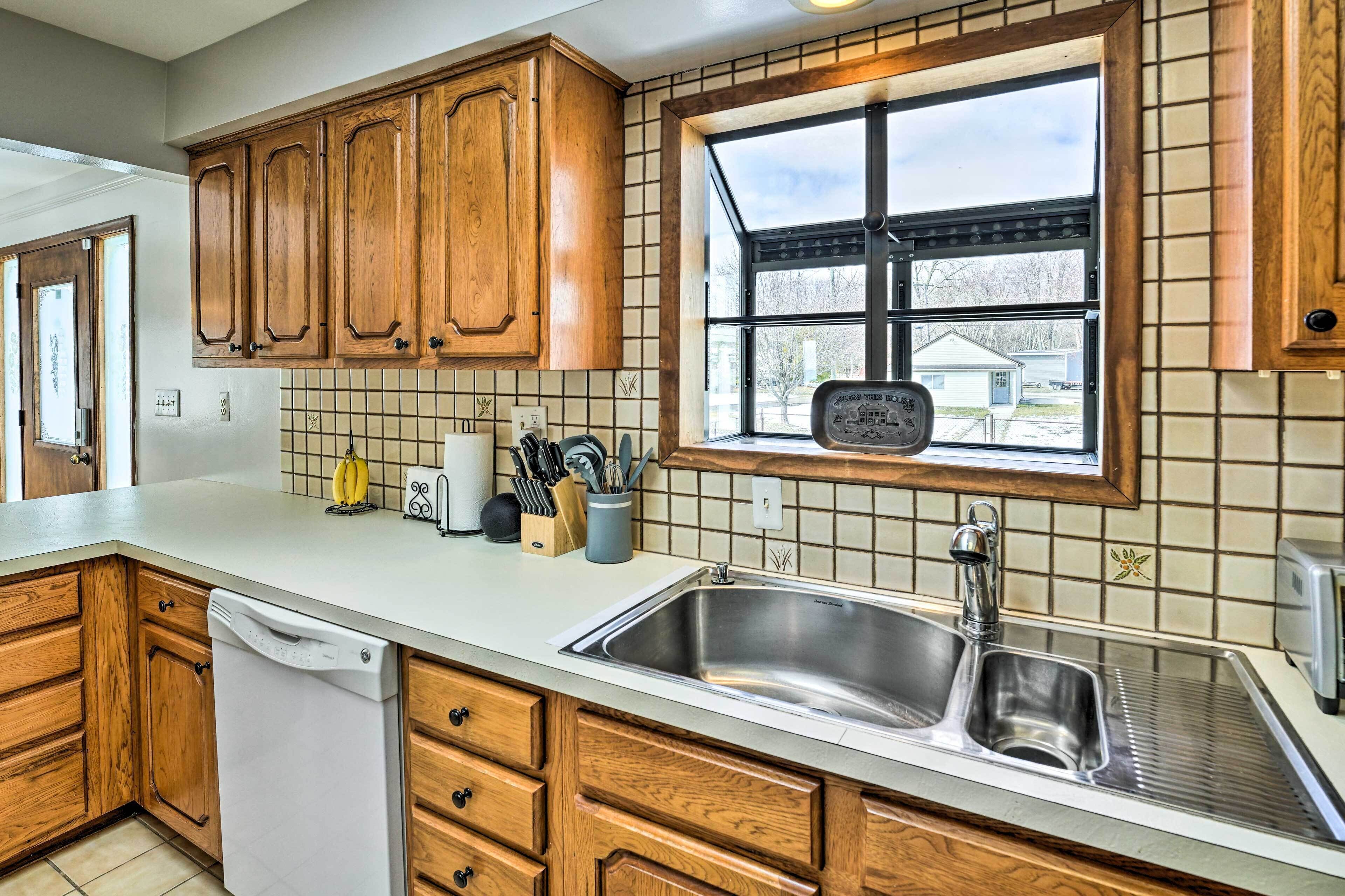A kitchen with wooden cabinets, a stainless steel sink, and a window with a view of houses.