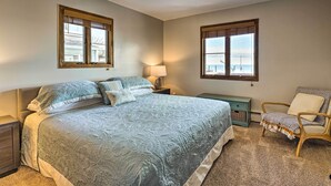 A bedroom with a large bed, two windows, a nightstand, a chair, and a lamp. - Anchor Bay Getaway on Lake St Clair With Dock! (New Baltimore)