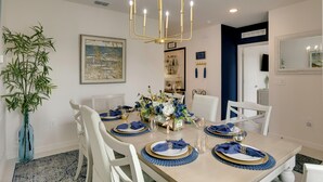 A dining room with a table set for six, featuring a chandelier, a vase with flowers, and a framed picture on the wall. - Beautiful Port St Lucie Home w/ Hot Tub! (Port Saint Lucie)