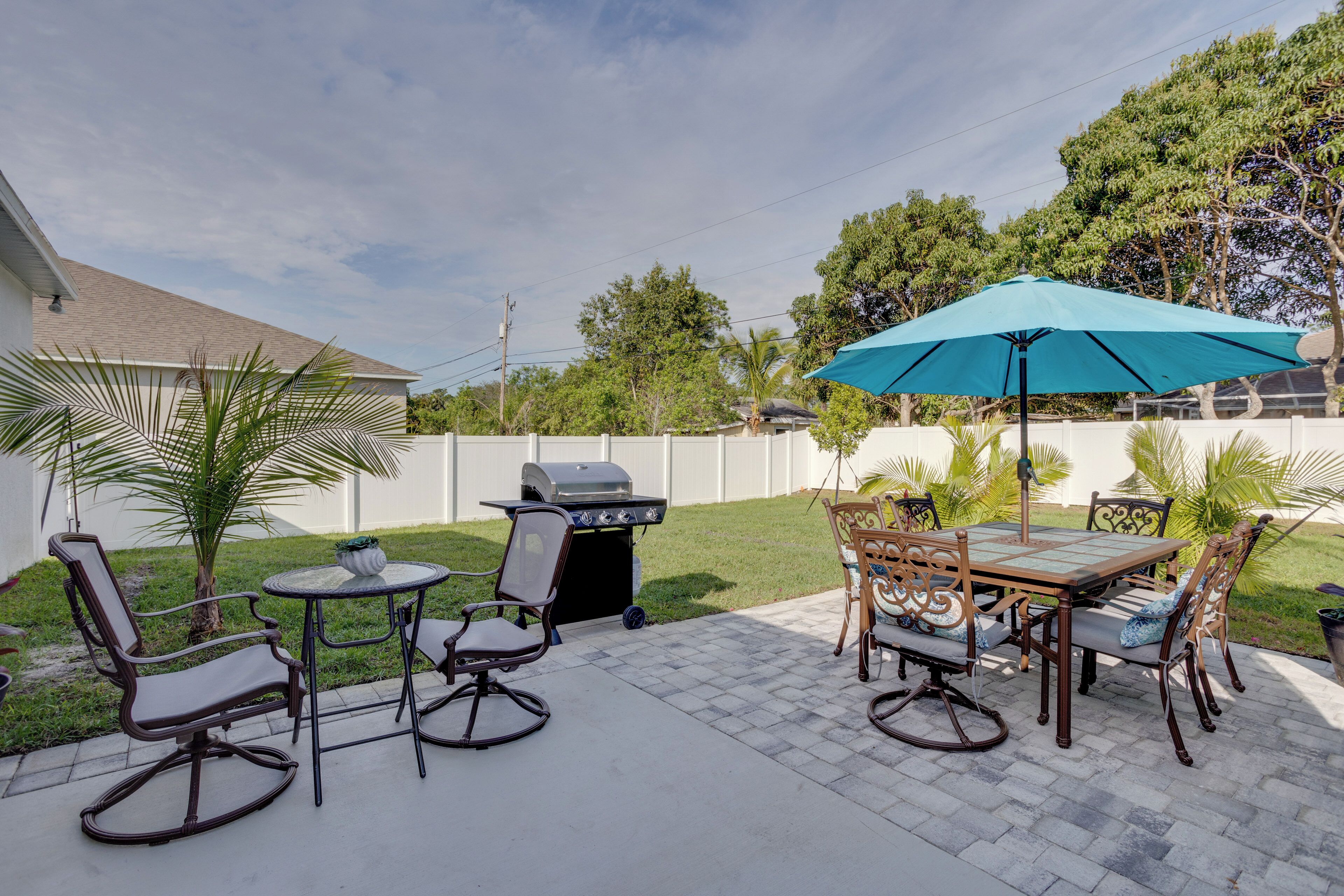 An outdoor patio with a grill, dining table, chairs, and a blue umbrella.
