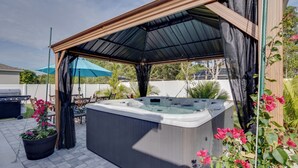 A hot tub under a wooden pergola with a metal roof, surrounded by potted plants and a patio area. - Beautiful Port St Lucie Home w/ Hot Tub! (Port Saint Lucie)