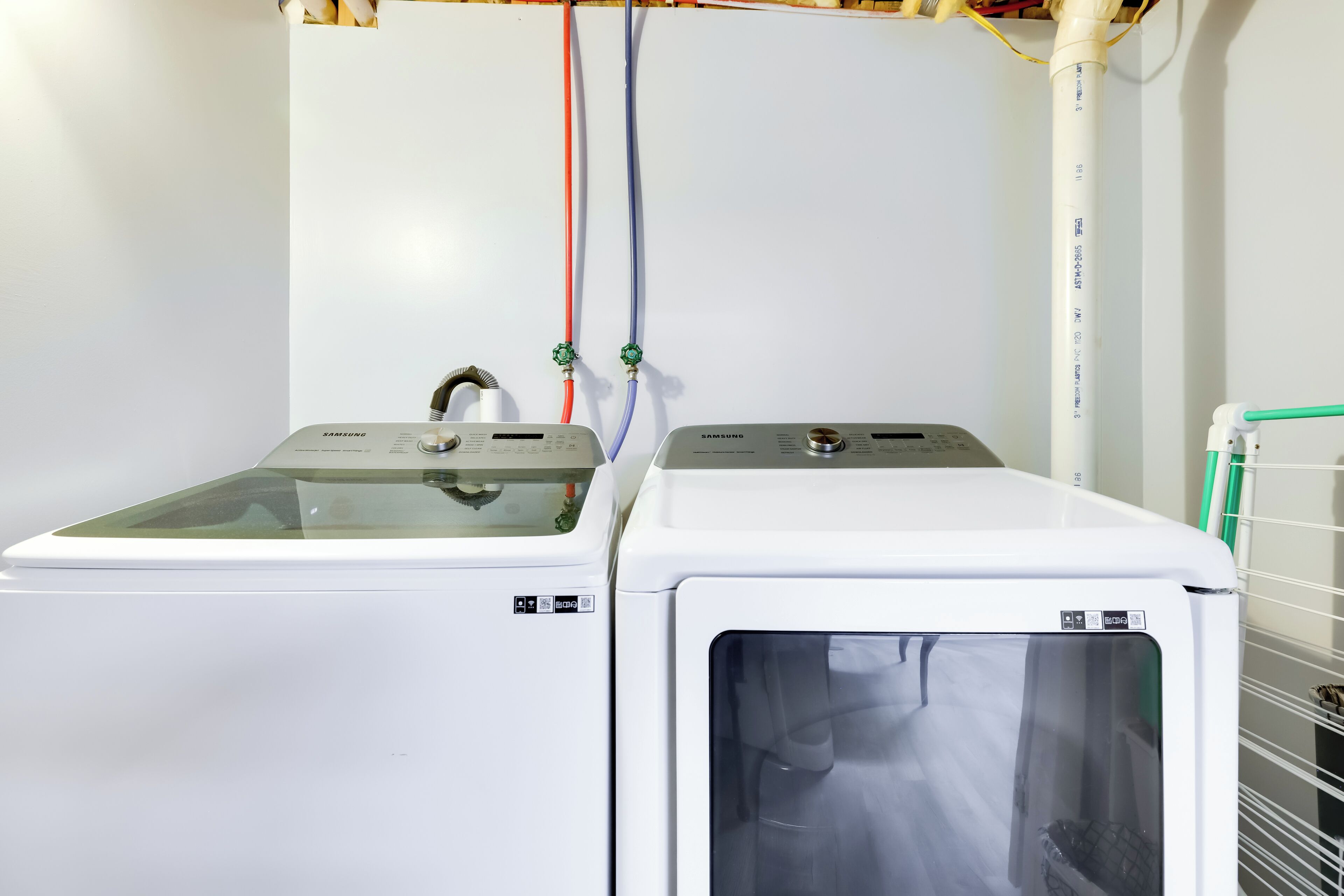 Deux machines à laver blanches, côte à côte, avec des tuyaux apparents et un mur blanc en arrière-plan.