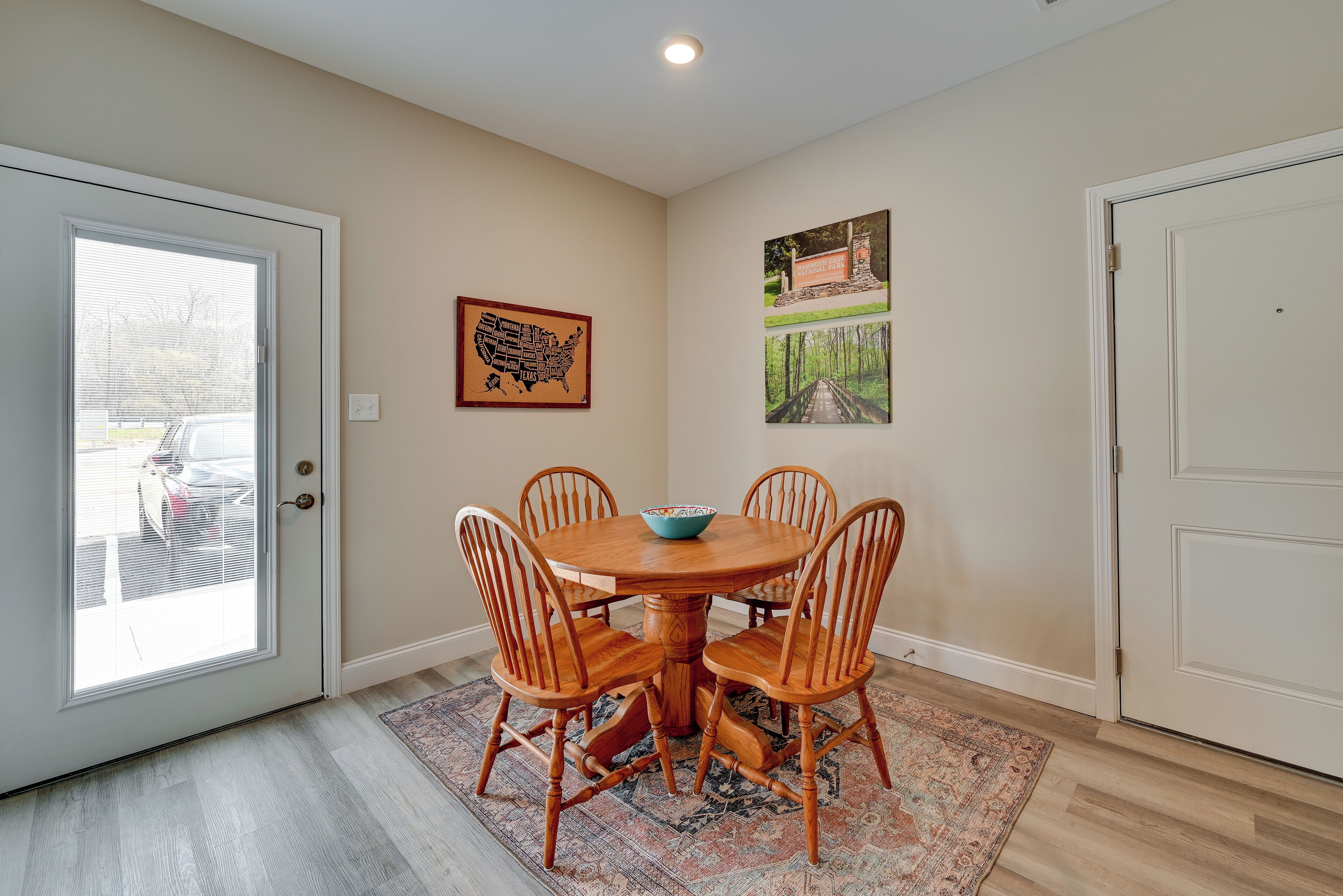 A dining area with a round table and four wooden chairs, a patterned rug, and two framed pictures on the walls.