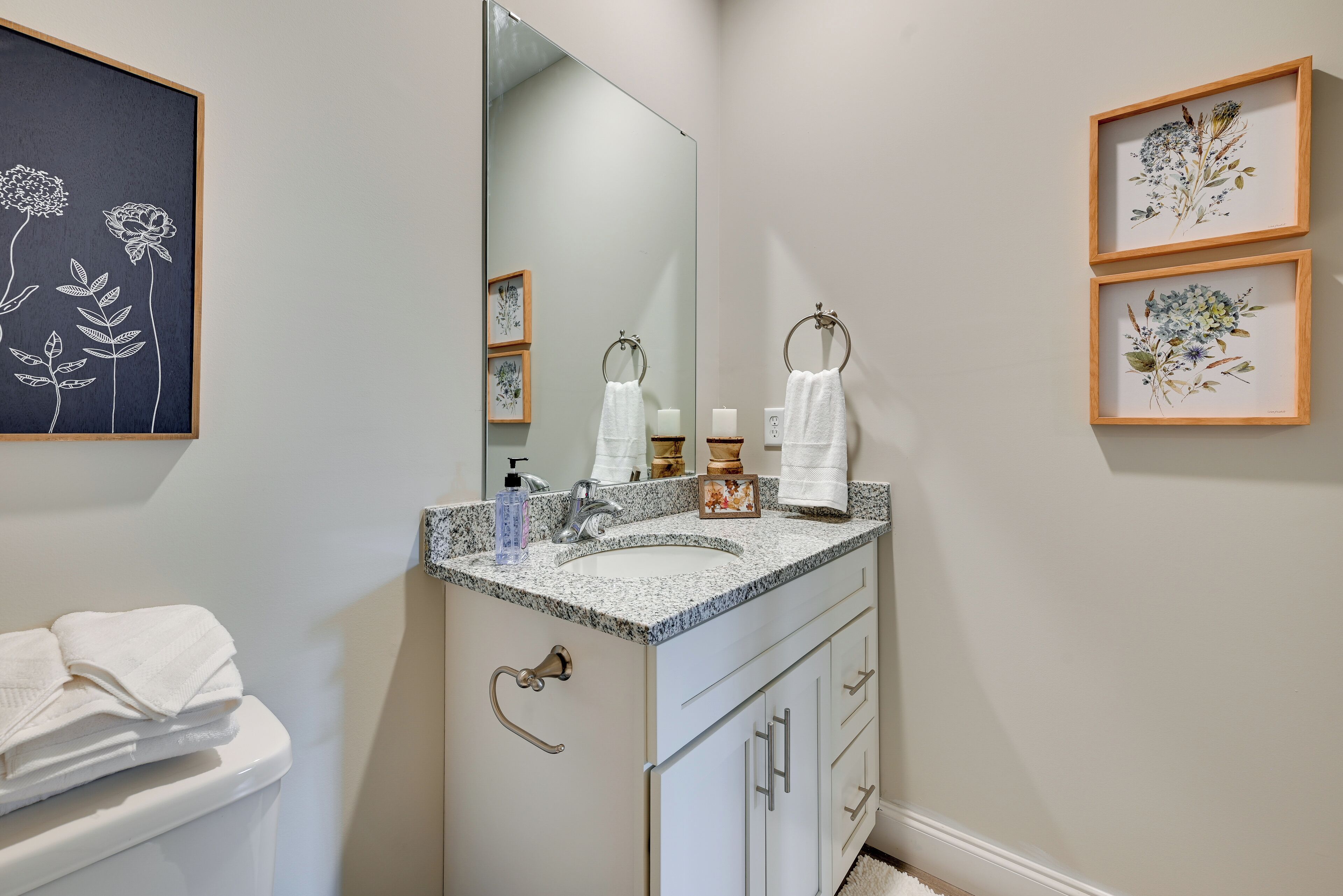A bathroom with a double sink, a large mirror, and framed floral artwork on the walls.