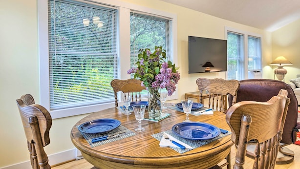 A dining area with a round wooden table set for four, surrounded by wooden chairs, a vase with flowers, and a flat-screen TV mounted on the wall. - 2 Bedrooms, Near Biking Trail, and Frankfort! (Frankfort)