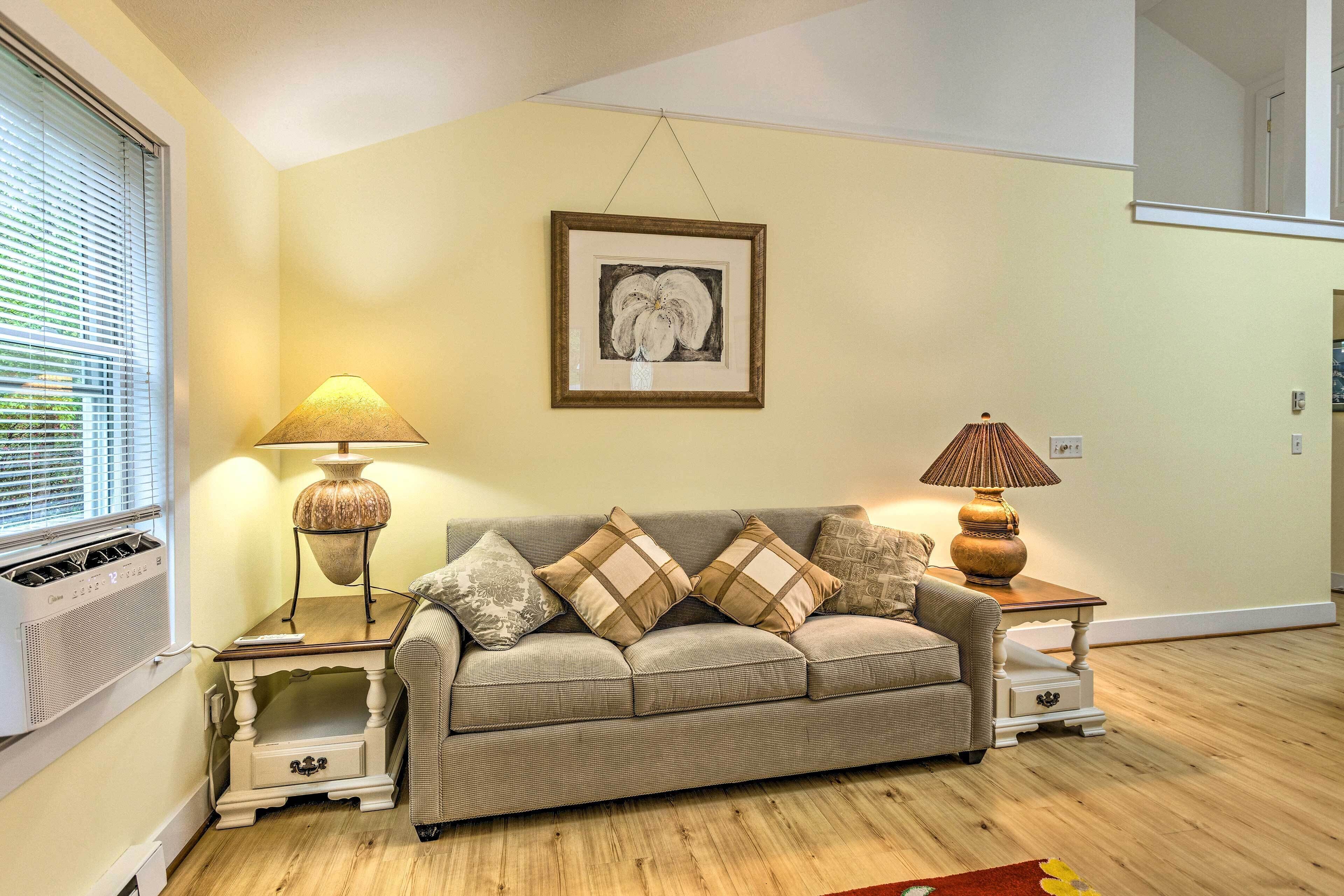 A living room with a beige sofa, two side tables with lamps, a framed artwork on the wall, and a window with blinds.