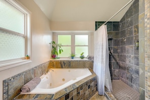 A bathroom with a large bathtub, a shower area, and a window with plants. - Hot Tub & Game Room: Spacious Live Oak Home! (San Antonio)