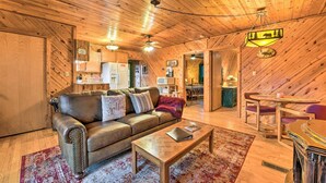 A cozy, wooden-floored living room with a leather sofa, a coffee table, and a dining area with a table and chairs. - Deck & Private Hot Tub! Maggie Valley Mtn Cabin (Maggie Valley)