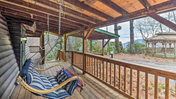 A wooden porch with a swing chair and a view of the surrounding landscape. - Deck & Private Hot Tub! Maggie Valley Mtn Cabin (Maggie Valley)