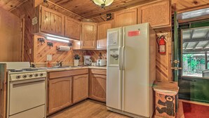 A kitchen with wooden cabinets, a stove, a refrigerator, and a coffee maker. - Deck & Private Hot Tub! Maggie Valley Mtn Cabin (Maggie Valley)