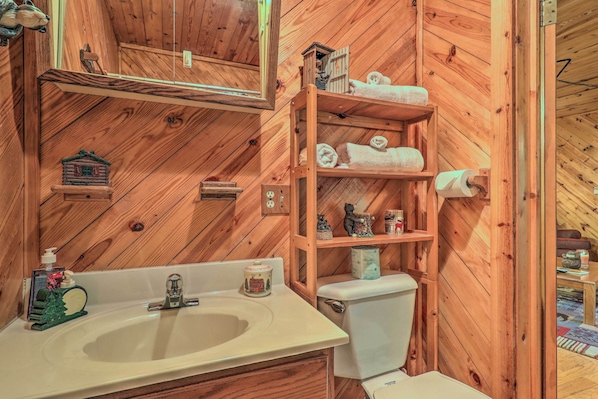 Un baño de madera con lavamanos, inodoro y repisas con toallas.