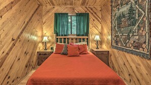 A cozy bedroom with a wooden ceiling, a large bed with red bedding, green curtains, and a tapestry on the wall. - Deck & Private Hot Tub! Maggie Valley Mtn Cabin (Maggie Valley)