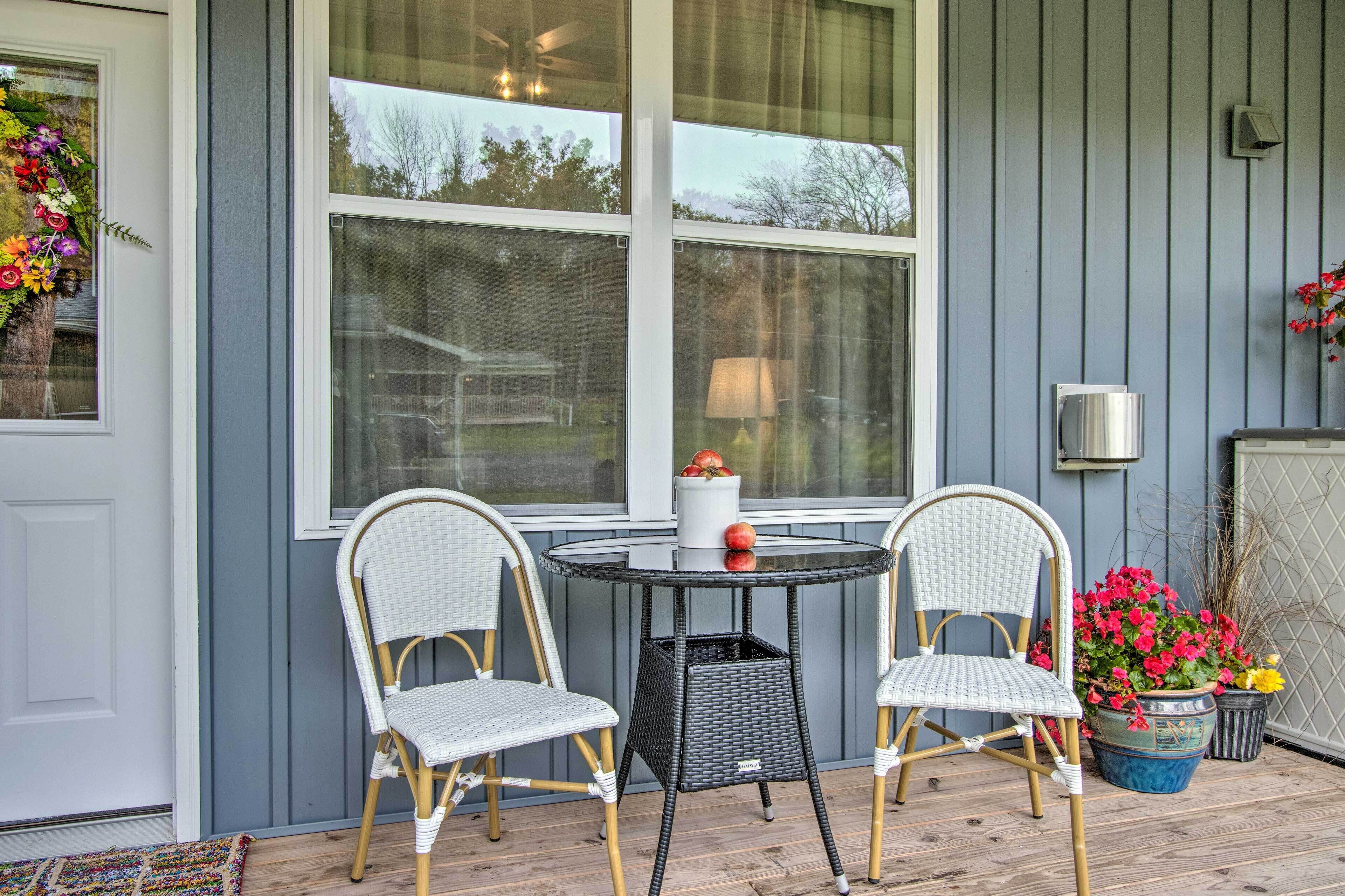 Une véranda avec deux fauteuils en osier, une petite table ronde et un pot de fleurs aux fleurs rouges.