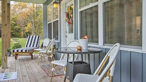 A covered porch with wicker furniture, a table with a vase, and a door decorated with a floral wreath. - Hike & Ski! Blue Heron Brodheadsville Cottage (Brodheadsville)
