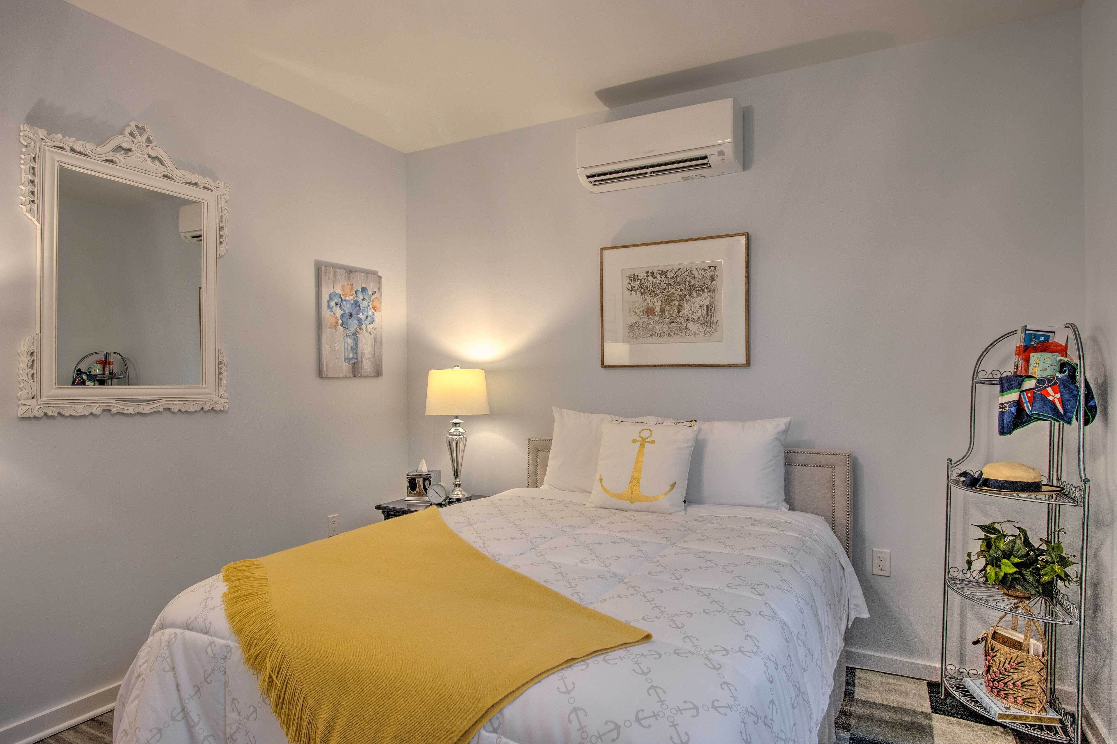 A neatly arranged bedroom with a bed, a bedside lamp, a mirror, and a wall-mounted air conditioner.
